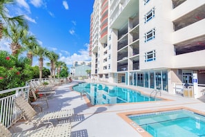 A hotel pool area with lounge chairs, a swimming pool, and a multi-story building with balconies.