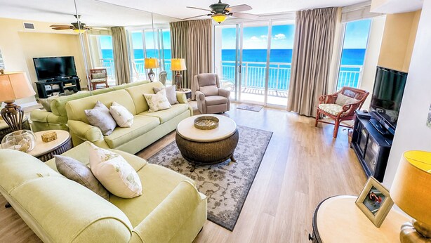 A spacious living room with a sofa, armchairs, a TV, and a balcony with a view of the sea.