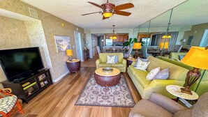 A spacious living room with a flat-screen TV, a ceiling fan, and a dining area visible through an open doorway.