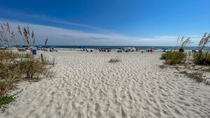 Una playa arenosa con huellas que conducen al agua, sombrillas y gente relajándose.