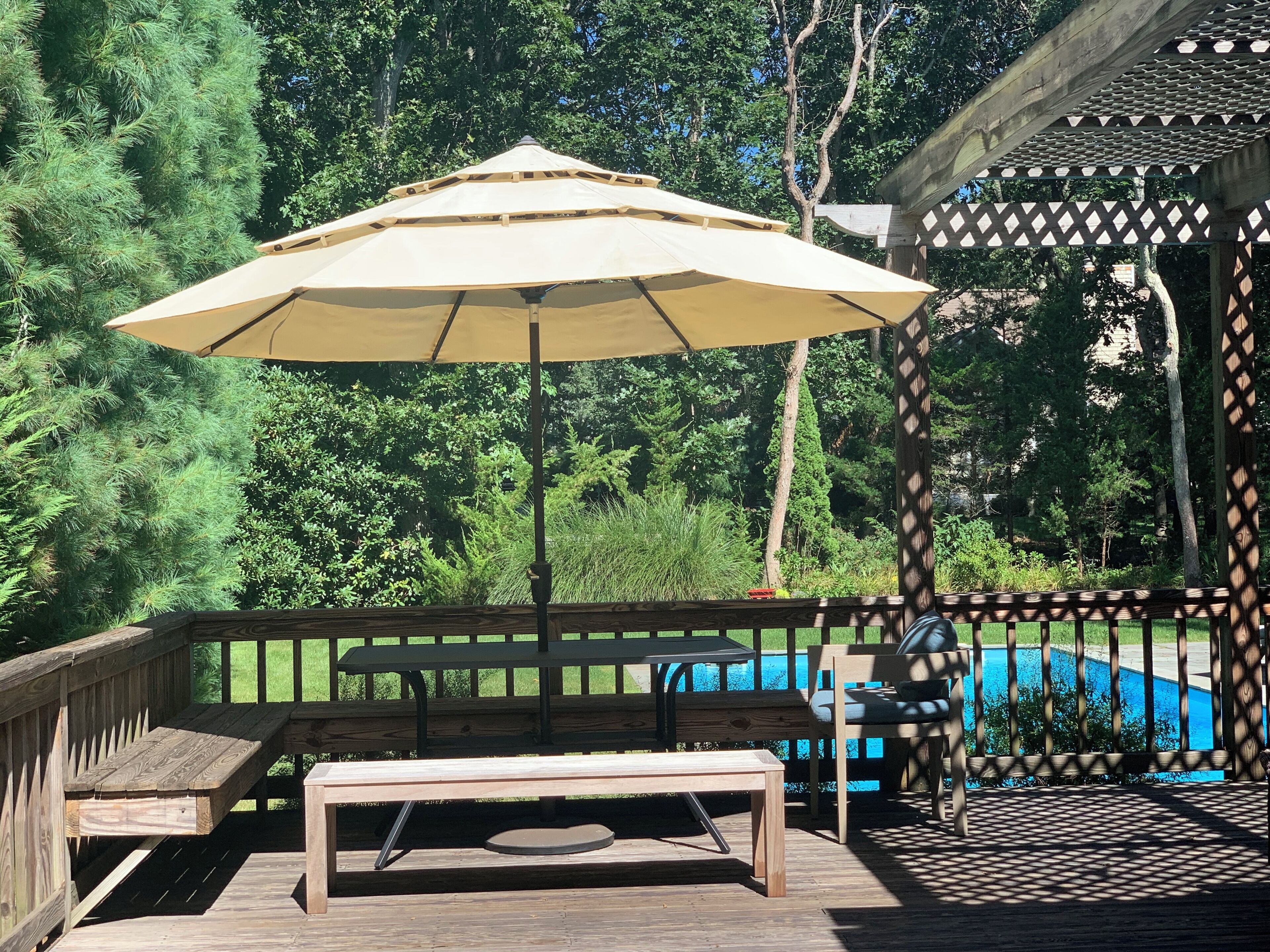 Une terrasse en bois avec une table et des chaises, une pergola et une piscine en arrière-plan.