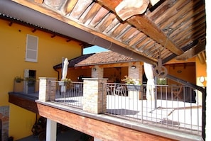 A wooden balcony with stone pillars, a tiled roof, and a yellow building in the background. - Agriturismo La Martina (Canelli)