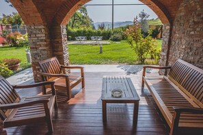 A wooden deck with a bench and chairs, a table, and a view of a garden and hills in the background. - Agriturismo La Martina (Canelli)
