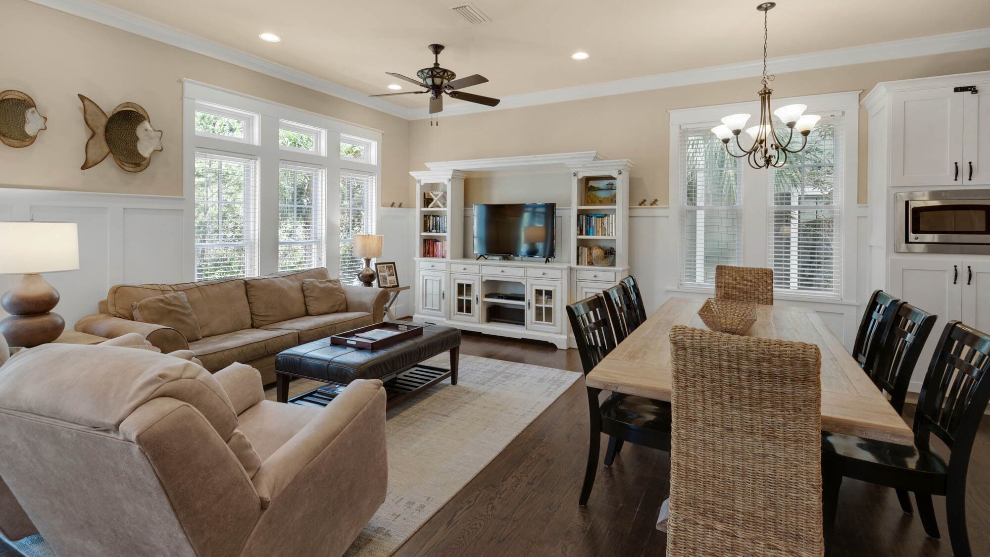 A spacious living room with a sofa, coffee table, and TV, a dining area with chairs and a table, and a kitchen with cabinets and appliances.