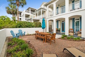 A multi-story building with balconies, a patio area with a wooden table and chairs, and a blue Adirondack chair. - Stay directly on 30A! Beautiful Beach House with private courtyard and panoramic views! Short walks to beach, pool, Rosemary and Alys! (Panama City Beach)