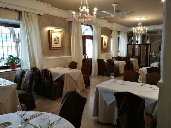 Un restaurante con varias mesas, cada una dispuesta con copas de vino y cubiertos, y un ventilador de techo.