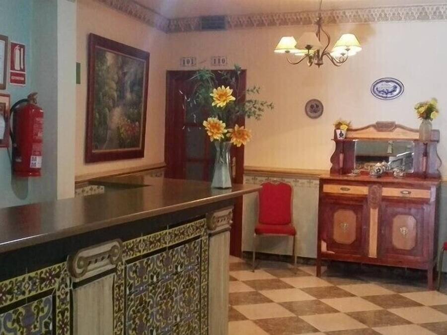 A reception area with a checkered floor, a reception desk, two red chairs, a vase with flowers, a fire extinguisher, framed certificates, and a painting on the wall.