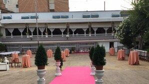 Un espacio para eventos al aire libre con alfombra rosa, mesas con manteles color melocotón y columnas decorativas blancas.