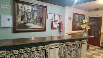 Een receptiezone met een balie, ingelijste kunstwerken, een brandblusser en een deur met kamernummers.