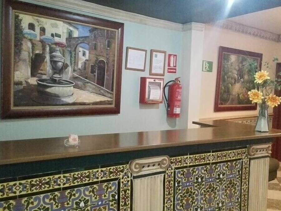 Een receptiezone met een balie, ingelijste kunstwerken, een brandblusser en een deur met kamernummers.