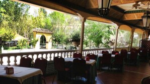 Un restaurante al aire libre con mesas y sillas, vista a zonas verdes y un techo decorativo.