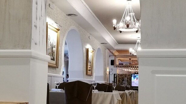 Un restaurante con una barra larga, techo abovedado y candelabros. Las mesas están dispuestas con copas de vino y manteles.