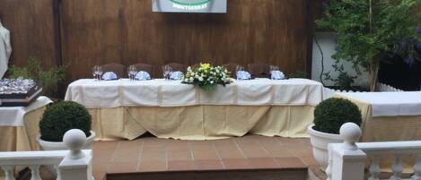 A covered outdoor seating area with a table set for a meal, a banner with the logo "AAA Montserrat", and steps leading up to the seating.