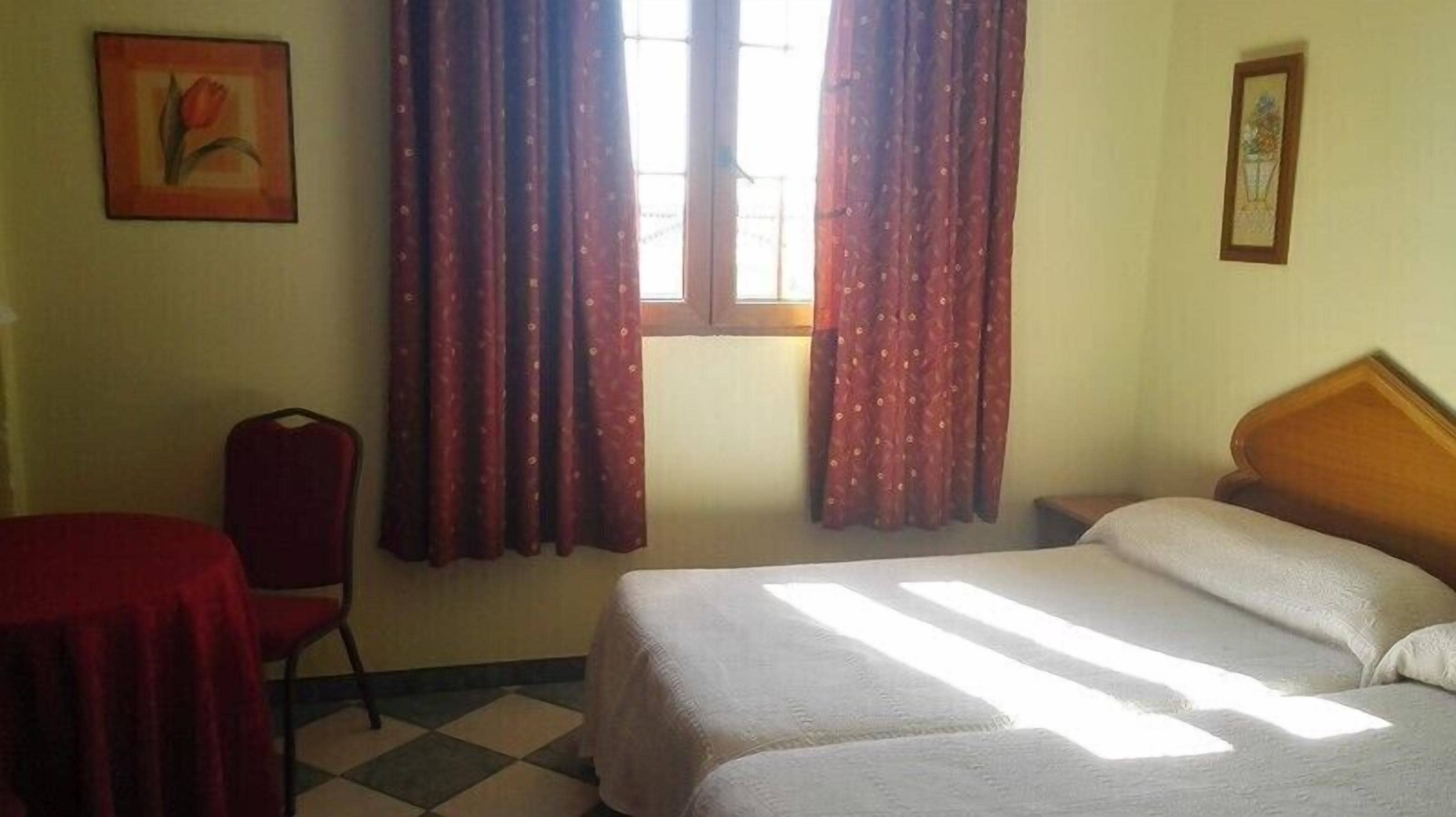 A room with two beds, a chair, a table, and curtains.