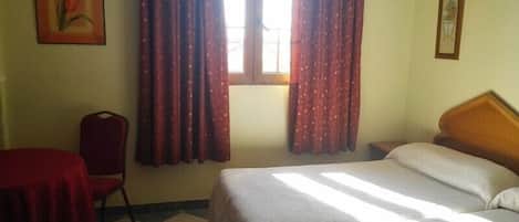 Una habitación con dos camas, una silla, una mesa y cortinas.