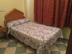 Una cama individual con una colcha estampada en una habitación con suelo a cuadros y cabecero de madera.