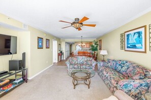 A living room with a ceiling fan, a sofa, a coffee table, and a television.