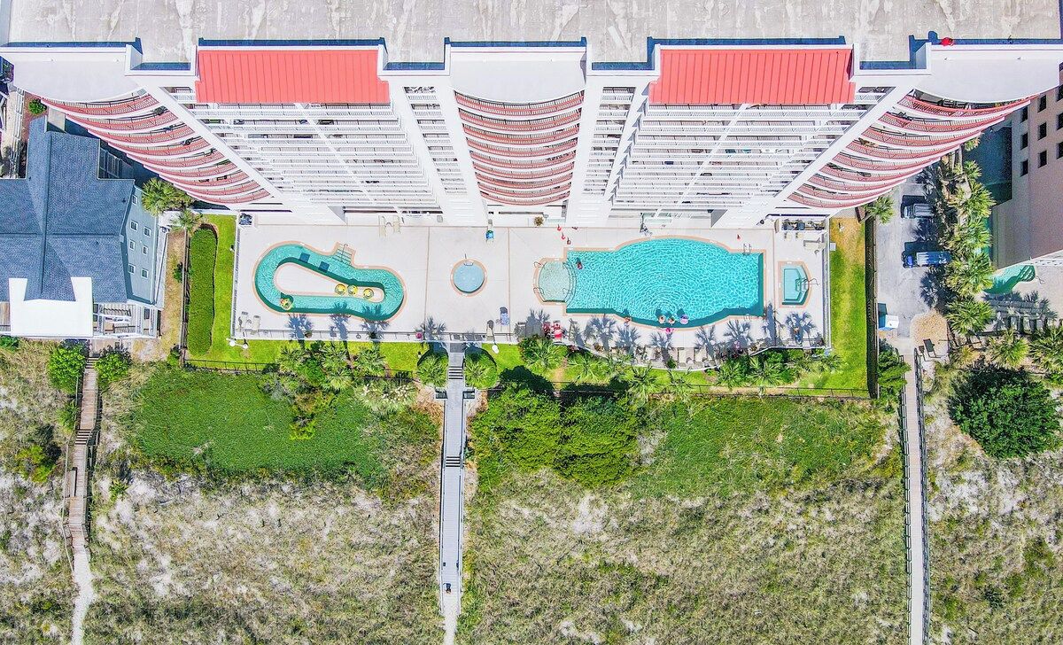 An aerial view of a hotel with multiple swimming pools, a central courtyard, and a modern architectural design.