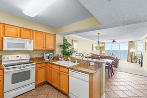 A kitchen with a microwave, stove, and dishwasher, a dining area with a table and chairs, and a view of the ocean.