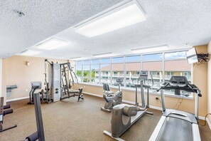 A gym with cardio machines, weight equipment, and large windows offering a view of buildings.