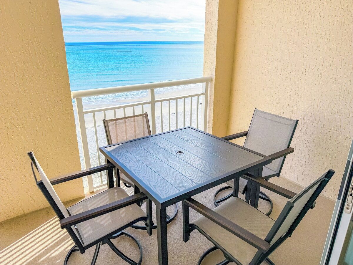 Un balcón con mesa y sillas, con vista a la playa.