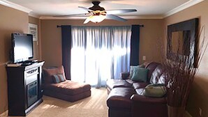 A living room with a ceiling fan, a television on a stand, a sectional sofa, and a large window with curtains. - Great NON-SMOKING, NO PETS ALLOWED..Easy to Get to, Short Drive To San Diego Fun (Bonita)