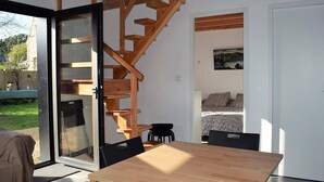 A modern interior with a wooden staircase, a dining area with a table and chairs, and a bedroom with a bed and a painting.