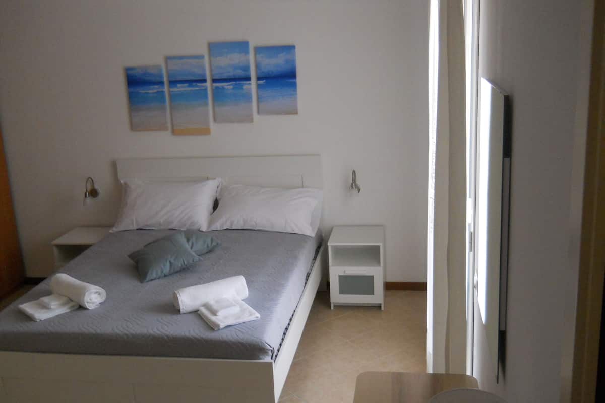 A neatly made bed with pillows and towels, a bedside table, a nightstand, and a wall with three framed pictures.
