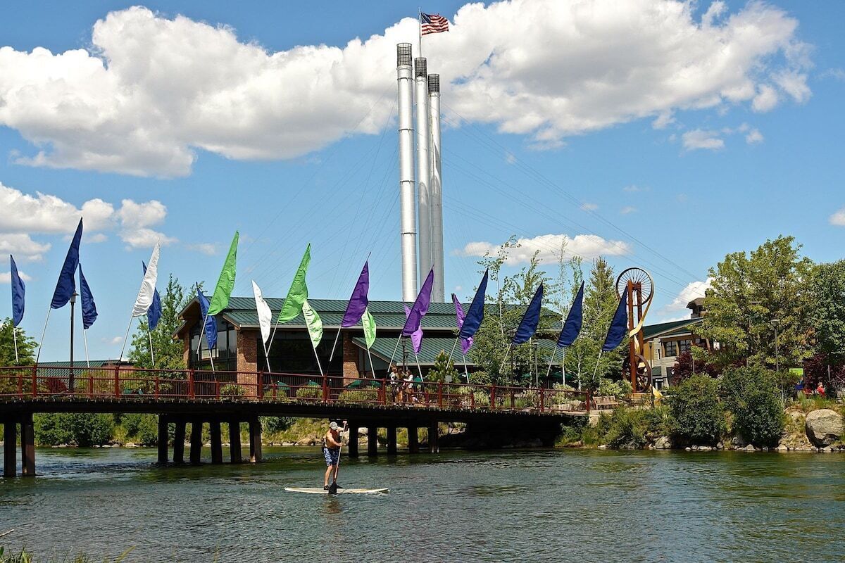 A pier with a person paddleboarding, a tall structure with an American flag, and colorful flags in the background.