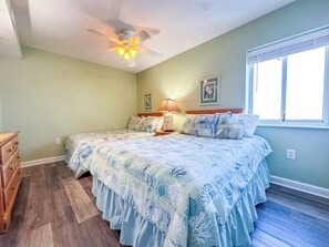 Une chambre avec deux lits, un ventilateur de plafond, une commode et une fenêtre.