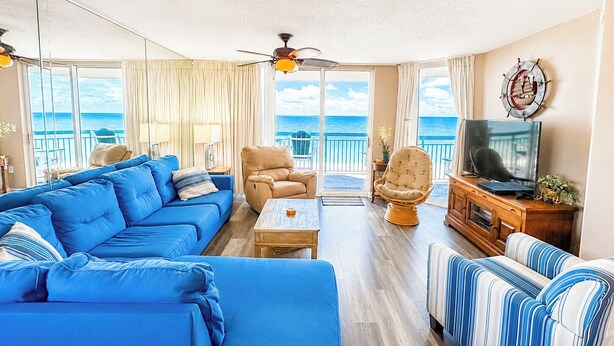 Una sala de estar con un sofá azul, un sillón color beige, una silla de mimbre, un televisor y vista al océano.
