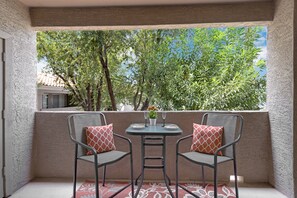 A balcony with two chairs and a table, featuring a view of trees and a building in the background. - Poolside Resort Style Awesomeness (Phoenix)