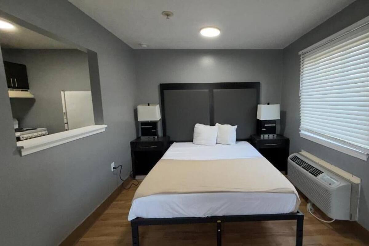 A bedroom with a bed, bedside tables, a mirror, and a window with blinds.