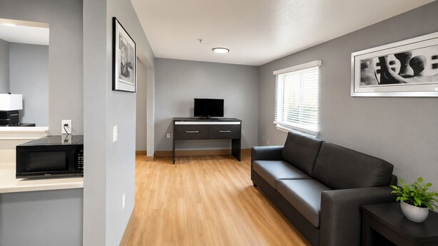 A modern living room with a flat-screen TV, a sofa, a coffee table, and a potted plant. - Welcome Suites Hazelwood (Hazelwood)