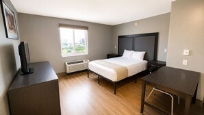 A hotel room with a bed, bedside tables, a desk, and a window with a city view. - Welcome Suites Hazelwood (Hazelwood)