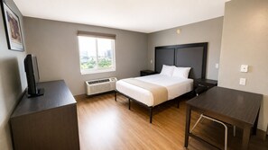A hotel room with a bed, bedside tables, a desk, and a window with a city view. - Welcome Suites Hazelwood (Hazelwood)