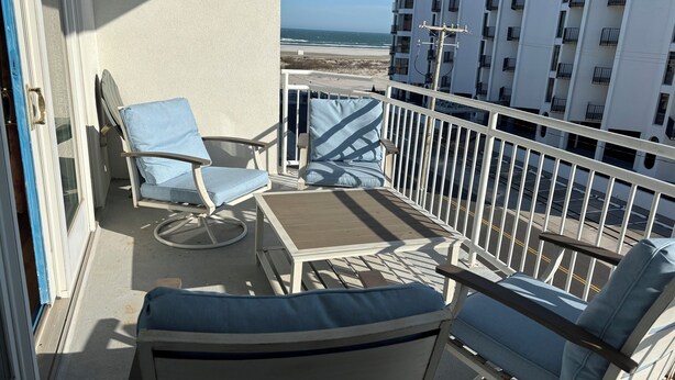 Varanda com vista para a praia, corrimão branco e duas cadeiras azuis.