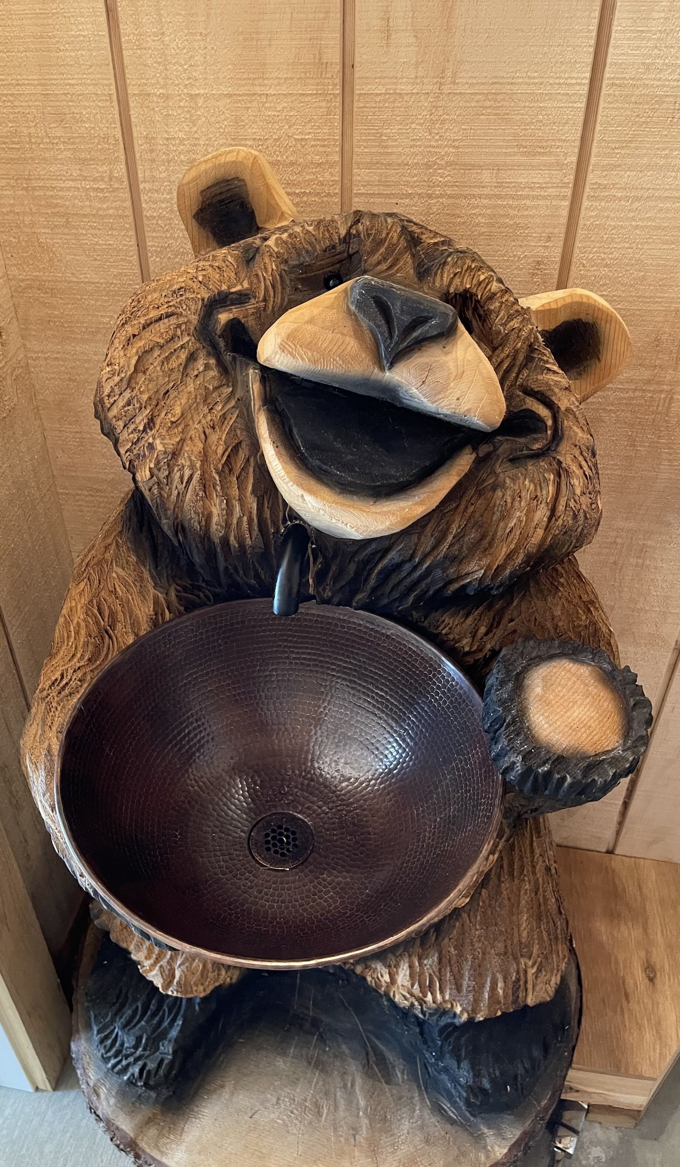 A wooden sculpture of a bear holding a large, dark bowl.