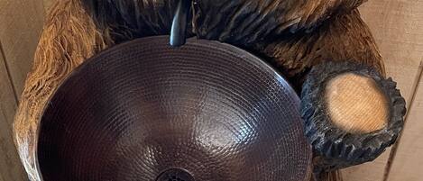 A wooden sculpture of a bear holding a large, dark bowl.