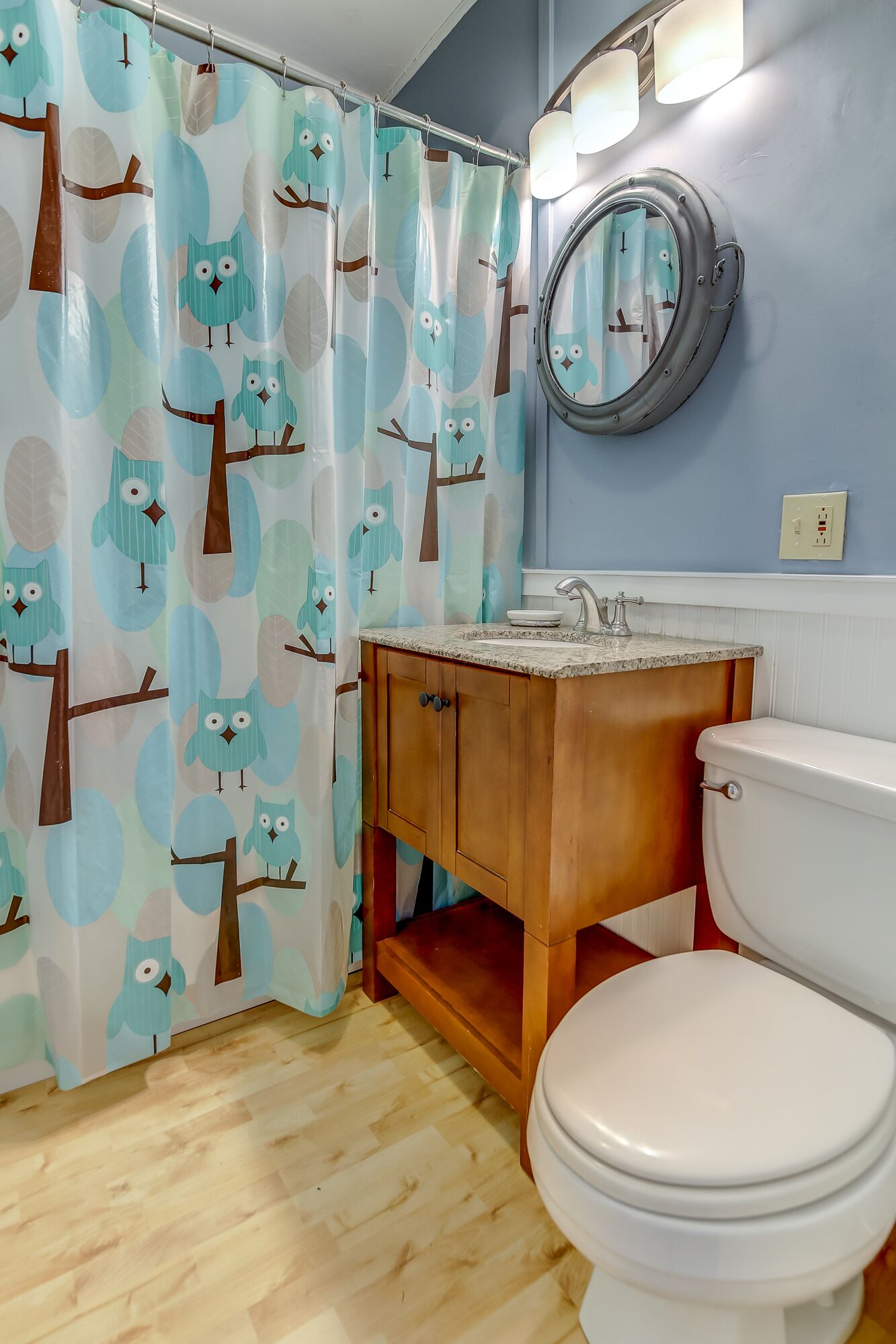 A bathroom with a toilet, wooden cabinet, and a shower curtain with owl patterns.