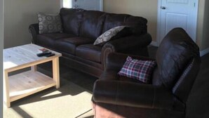 Sala de estar com um sofá de couro marrom, mesa de centro de madeira e almofada xadrez.