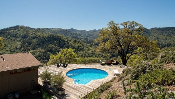 A swimming pool with a wooden deck, surrounded by lush greenery and hills in the background.
