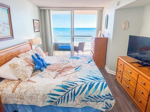 Una habitación de hotel con cama, televisión, cómoda y balcón con vista al océano.