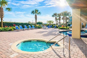 A pool area with lounge chairs, a hot tub, and palm trees.