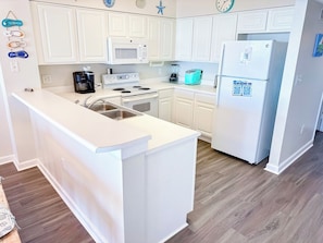 A kitchen with white cabinetry, a built-in microwave, a stove, a sink, and a refrigerator.
