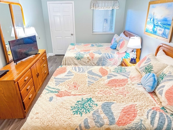 A bedroom with two beds, a wooden dresser, a desk with a computer, and a painting on the wall.
