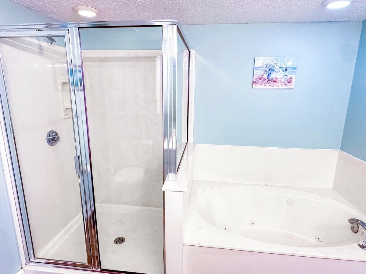 A bathroom with a glass shower enclosure and a white bathtub.