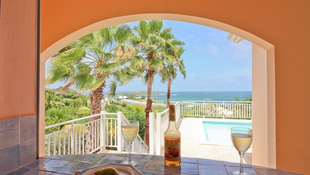 A balcony with a view of the ocean, a bottle of wine, and two glasses. - Luxurious Caribbean Contemporary Charm with Breathtaking Panoramic Ocean View (Cul-de-Sac)