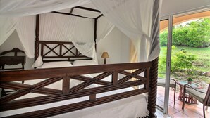A bedroom with a four-poster bed, a nightstand, a lamp, and a view of a garden through a glass door. - Luxurious Caribbean Contemporary Charm with Breathtaking Panoramic Ocean View (Cul-de-Sac)