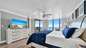 Ein Schlafzimmer mit Bett, Kommode, Deckenventilator und einem großen Fenster mit Meerblick.